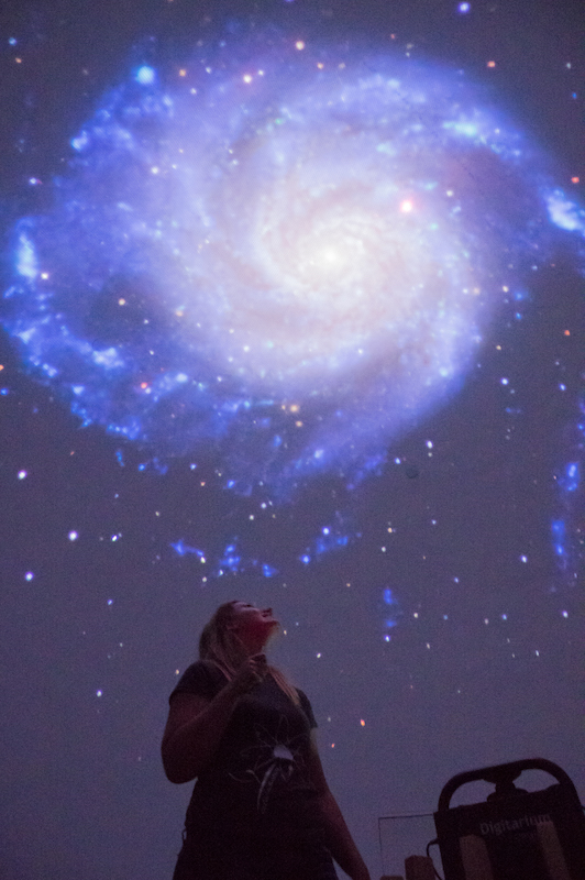 Photo of Chelsea Sharon in the McCallion Planetarium pointing out features in an image of a spiral galaxy.